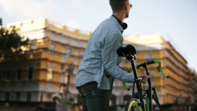 穿着休闲服和太阳镜的英俊年轻白人男子在城市上楼时，肩上扛着一辆自行车。罕见的低角度镜头