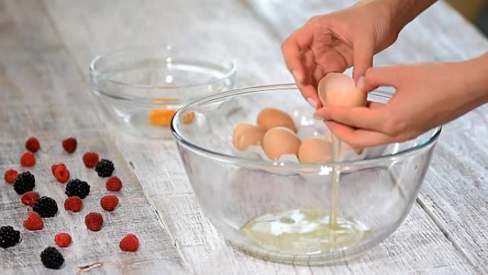女人的手打碎鸡蛋以分离蛋清，蛋黄和蛋壳的背景。