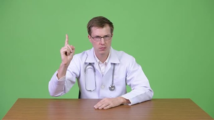 年轻男子医生坐在手指向上的肖像