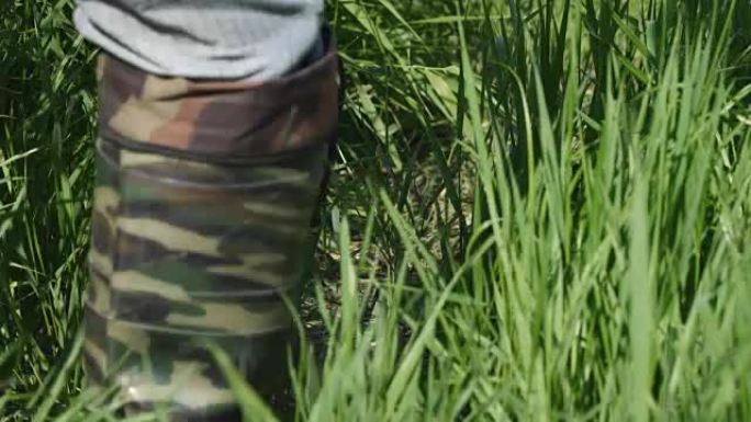男子穿着保护色的卡其色靴子沿着茂密的草丛行走