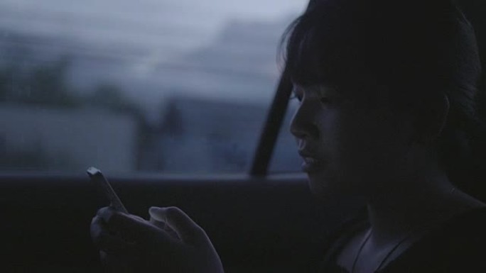 一个晚上在车里玩智能手机的亚洲女人。