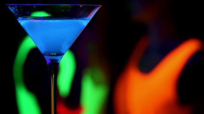 蓝色发光饮料与跳舞的女人在紫外线发光派对背景。。