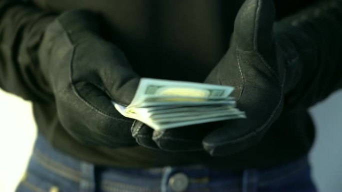 犯罪概念男子穿着黑色皮手套拿着一堆钱