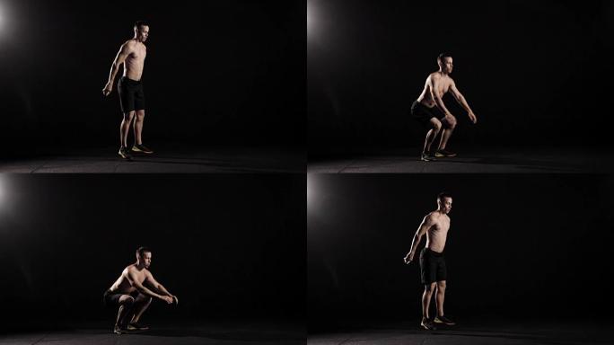 健身模特光着上身在黑暗的工作室里做下蹲跳