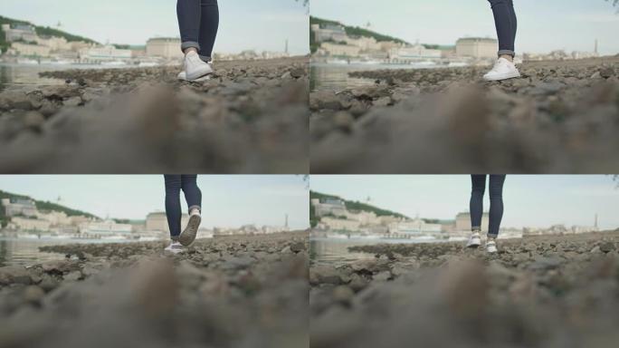 苗条女孩的脚在河边的岩石上行走