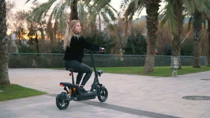 漂亮的金发女人在城市公园驾驶电动自行车