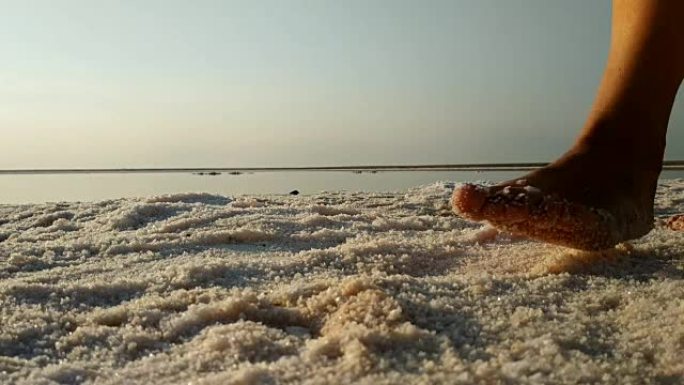 赤脚走在粉红湖盐岸的女孩。