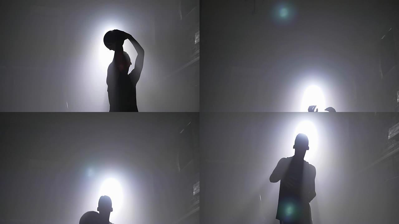 篮球运动员剪影在篮筐里扔球，到处都是烟，背景是泛光灯