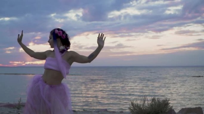 可爱的女人，穿着粉红色的连衣裙在河岸上跳舞，妆容闪闪发光。一个性感女孩的舞蹈，有着美妙的发型和鲜花。