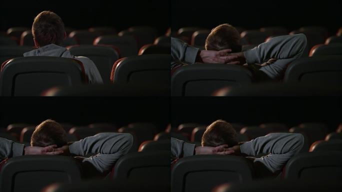 一个人坐在空荡荡的电影院里。年轻人在空旷的黑暗剧院中放松