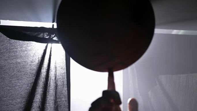 篮球运动员手指上旋转的球的近距离镜头，带泛光灯的黑暗迷雾房