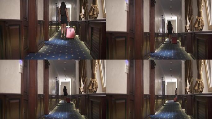 一个黑发女人带着拉杆箱沿着酒店走廊散步的后视图。摄像机自底向上移动