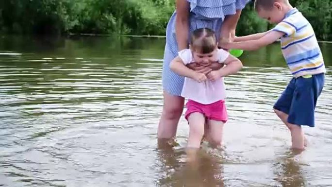 小女孩的母亲在河里洗脚。一个女人和她的孩子站在水里