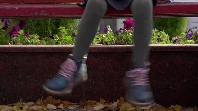 女童坐在长凳上摇晃双腿。儿童脚的特写。秋天的日子。