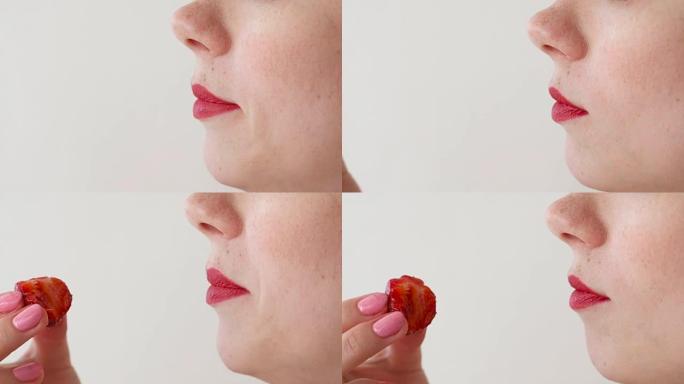 嘴唇红红的女人吃草莓。嘴巴特写。侧视图。
