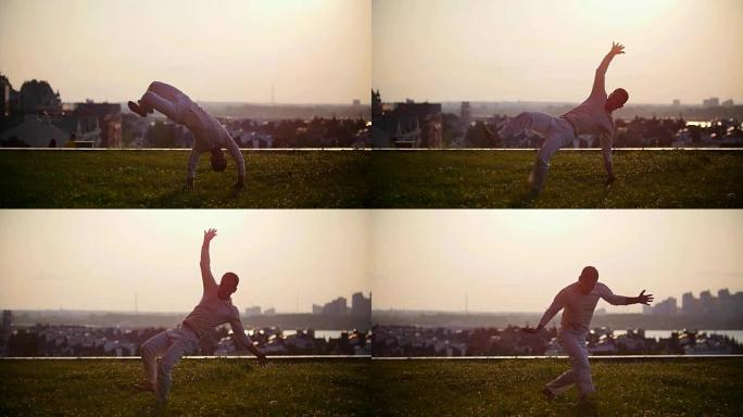 运动男子在城市景观和美丽的日落背景下展示卡波耶拉舞蹈的酷把戏