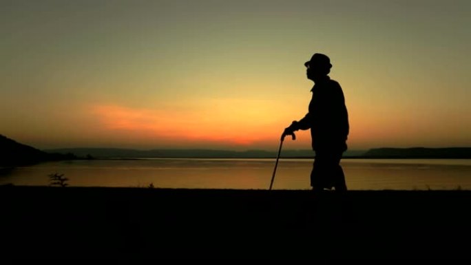 老年亚洲男性在湖边日落时用棍子行走，概念健康，慢动作