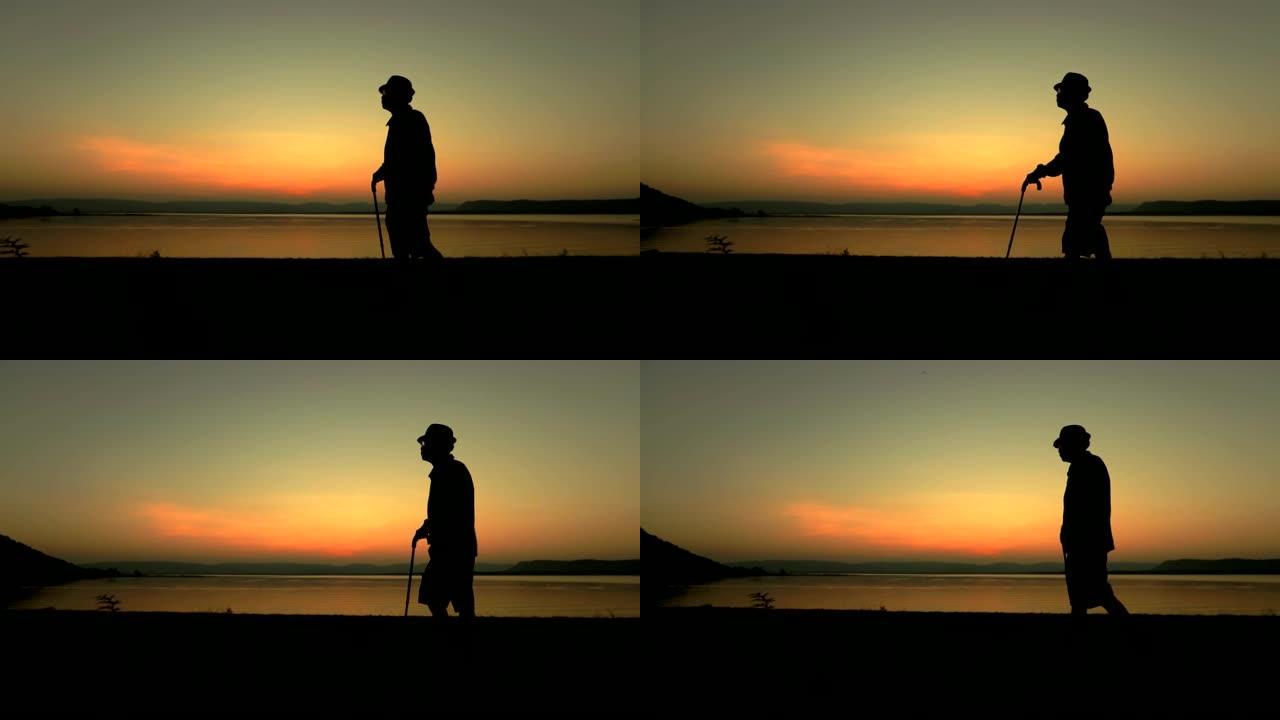 老年亚洲男性在湖边日落时用棍子行走，概念健康，慢动作