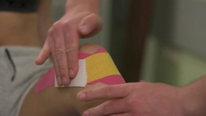 放在膝盖上的双手摩擦kinesiotape的特写镜头。如果前十字韧带受伤，治疗师会对膝关节进行运动。