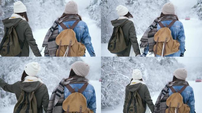 冬天，两个微笑的女人在公园散步。背着背包的朋友穿过森林。在白雪皑皑的森林背景下，穿着针织帽和冬装的女