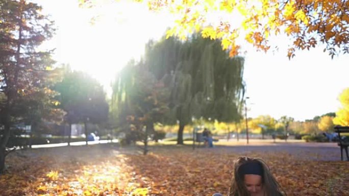 可爱的女孩在秋天的城市公园里奔跑和摔倒