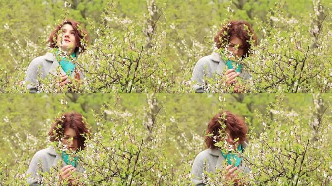 漂亮浪漫的年轻红头女人，樱桃枝在春天公园开花。春天的树背景。肖像特写。