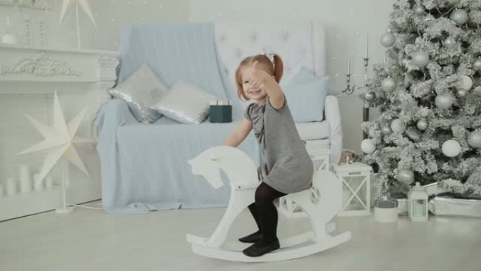 非常漂亮的小女孩在新年的房间里骑着一匹木马，微笑着