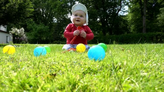 男婴坐在草地上，在五颜六色的球之间玩耍。4K
