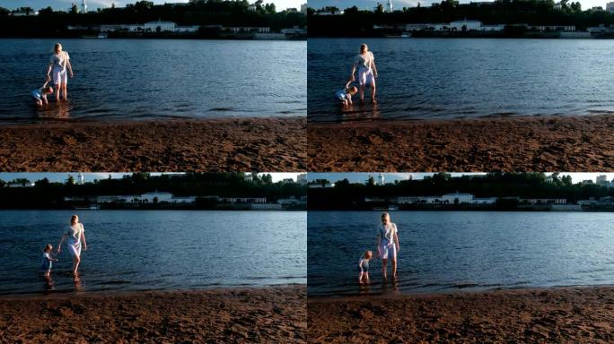 妈妈和女孩在日落时在河边的海滩上玩耍，游泳。