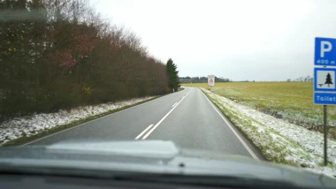 挡风玻璃上的视频。汽车在柏油路上行驶。雪覆盖绿草。路标。丹麦