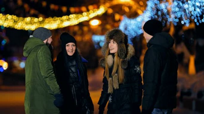 朋友们在美丽的冬季街道上谈笑风声。男孩和女孩很开心，他们在微笑。摄像机的侧面跨度。