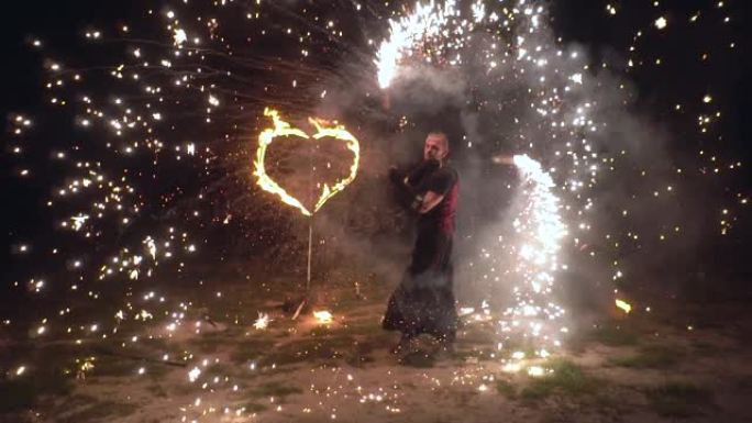 Fire show man艺术家在他的手中以燃烧的心在背景上扭曲火物