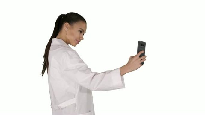 时尚的欧洲布鲁内特医生在白色背景上行走时在手机上自拍