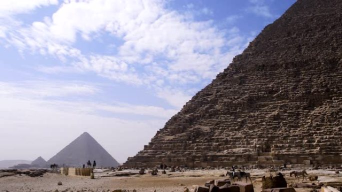 埃及吉萨金字塔。我们可以看到云朵在联合国教科文组织分类的纪念碑上方，埃及人在金字塔前行走。