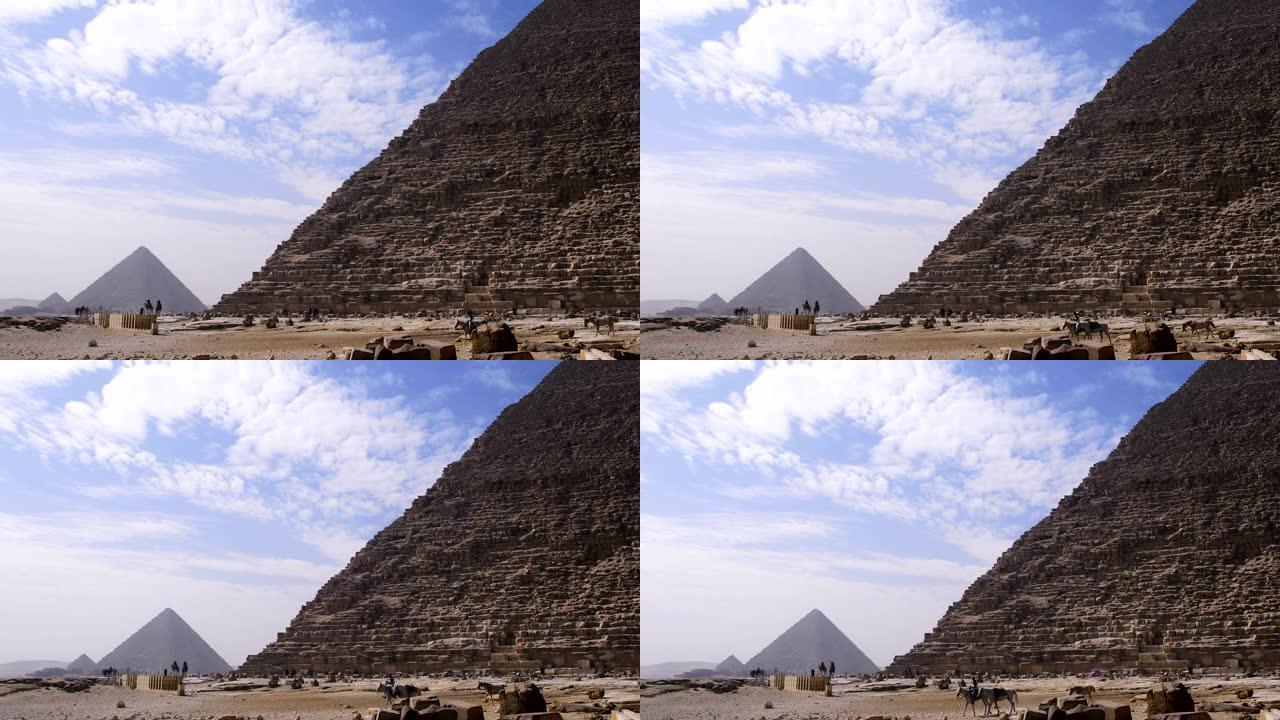 埃及吉萨金字塔。我们可以看到云朵在联合国教科文组织分类的纪念碑上方，埃及人在金字塔前行走。