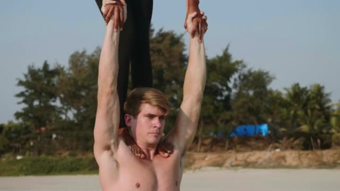 适合运动情侣在沙滩上与伴侣一起练习acro瑜伽。