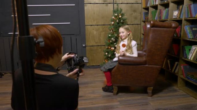 美国巴尔的摩-2018年12月25日: 少女在书柜和照相馆的圣诞树上，坐在皮革扶手椅上摆姿势。在新年