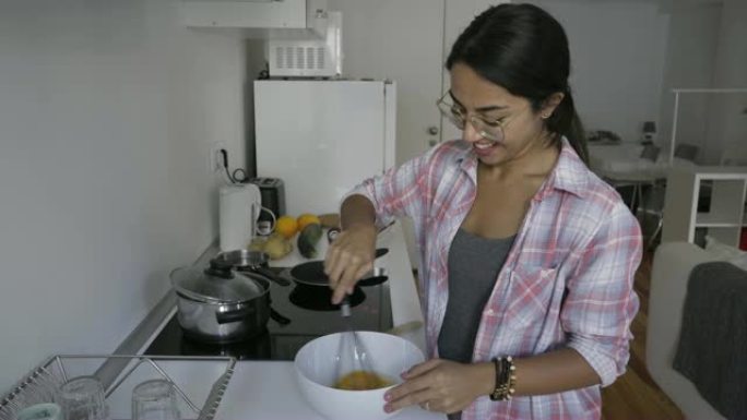 微笑的黑发女人戴着眼镜在厨房打鸡蛋。