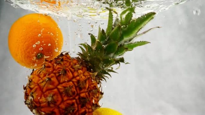 菠萝，橙子和柠檬以慢动作飞溅和气泡落入水中。