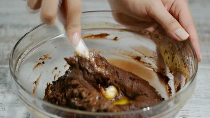 女孩用抹刀搅拌巧克力面团。制作巧克力面糊的过程。