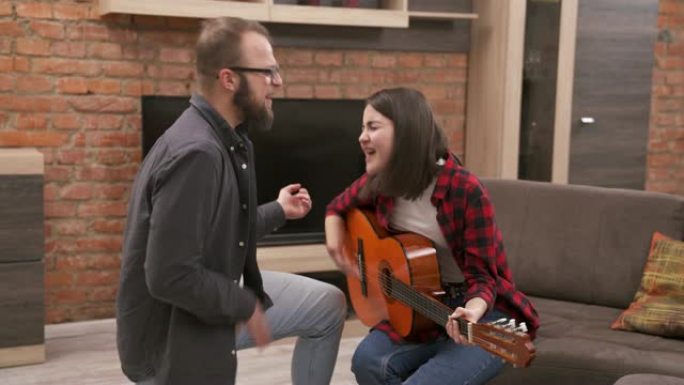 一对年轻夫妇玩得很开心，一起唱歌，女孩坐在沙发上弹木吉他，男友模仿弹