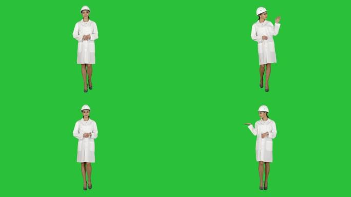 戴安全帽的成熟工程师妇女在绿色屏幕上行走时用手指示产品或文字，色度键