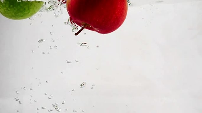 绿苹果和红苹果随气泡落入水中的慢动作视频。孤立背景上的水果。