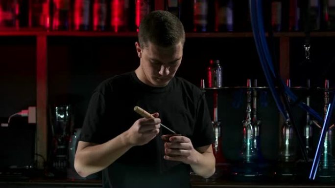 一个男人在碗里为酒吧的水烟准备水果烟草。慢动作。
