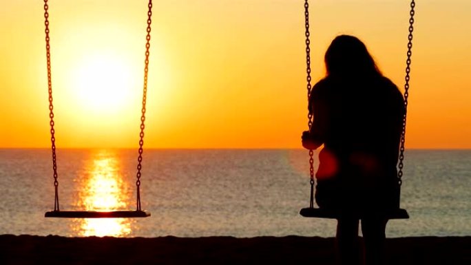 悲伤的女孩在日落时在海滩上摇摆