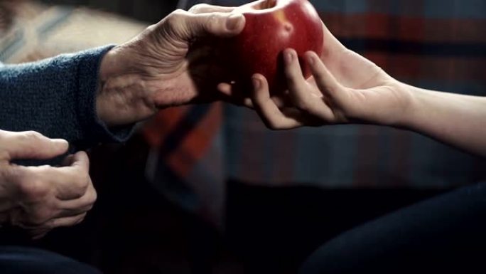 一个老妇人的手把一个红苹果递给一个少年