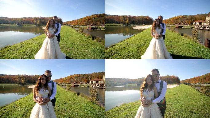 新娘在湖边的公园里跳舞。阳光明媚的日子，这些漂亮的新娘在壮丽的湖边的桥上跳舞
