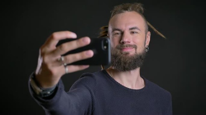 怪异的高加索人与辫子和穿孔制作水平自拍-使用黑色背景上的智能手机照片。