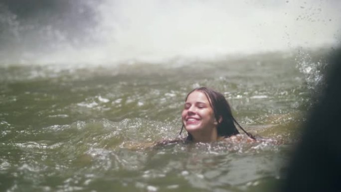 美女在山湖游泳，水花在背景上。旅游妇女沐浴在热带森林山瀑布的淡水中。
