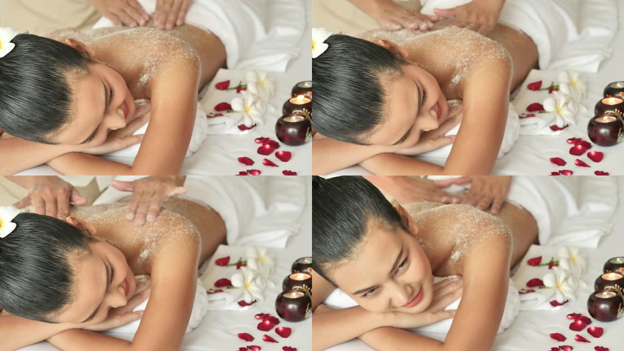 年轻的亚洲女人躺在床上放松地擦洗身体。按摩师，盐磨砂美容治疗在健康水疗。4k视频慢动作